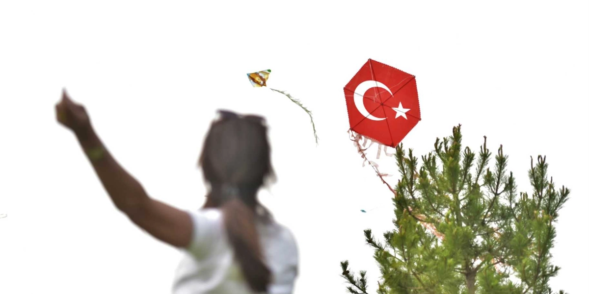 Beyaz bir gökyüzüne karşı, arkası dönük bir kadın elini havaya kaldırarak uçurtmaları izliyor. Gökyüzünde üzerinde Türk bayrağı deseni bulunan altıgen bir uçurtma ve yanında daha küçük, renkli bir uçurtma süzülüyor. Sağ tarafta ise yeşil bir çam ağacının tepesi görünüyor.