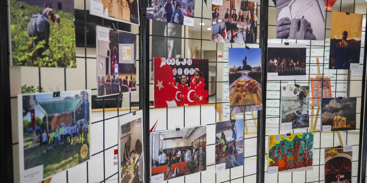 Siyah metal bir tel pano üzerine mandallarla tutturulmuş, Bornova'daki çeşitli etkinlikleri ve sosyal yaşamı yansıtan çok sayıda fotoğraf karesi. Fotoğraflar arasında elinde kalemle yazı yazan yaşlı bir el, Türk bayrakları tutan çocuklar, bir toplantı anı, açık hava etkinlikleri, bir dokuma tezgahı başında çalışan kadın, tarihi yapılar, bir köpek ve çocukların yaptığı renkli resimler yer alıyor. Pano, sergi alanında bir bölme görevi görüyor ve arka planda sergi mekanının iç mekanı seçiliyor.