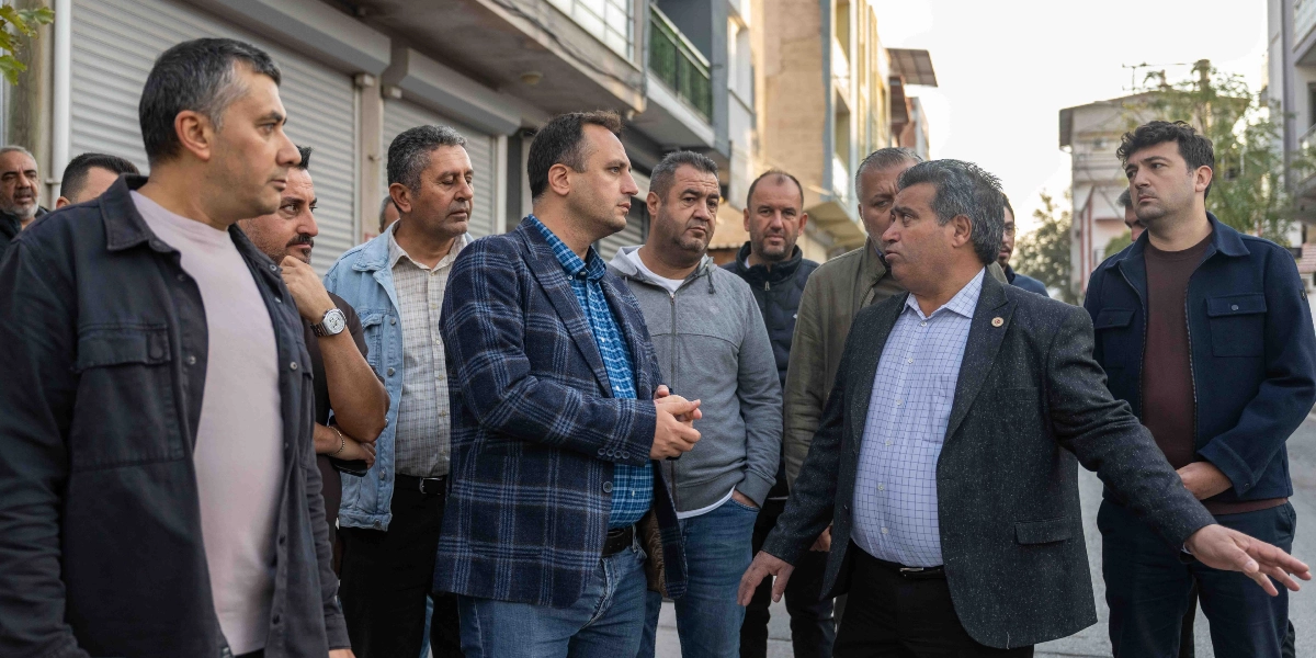 Bornova'da bir sokakta bir araya gelen bir grup erkek, çevreyi inceleyerek fikir alışverişinde bulunuyor. Grubun önünde yer alan, üzerinde kareli ceket ve gömlek olan bir kişi eliyle sokağı işaret ederek açıklamalarda bulunurken, yanındaki diğer kişiler dikkatle onu dinliyor.
