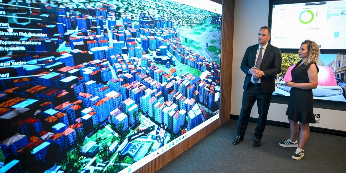 Takım elbiseli bir erkek ve siyah elbiseli bir kadın, Bornova'nın dijital üç boyutlu şehir modelinin yansıtıldığı dev bir ekranın önünde duruyor. Ekranda binaların risk durumları, toplanma alanları ve sosyal yardım gibi verilerin yer aldığı bir arayüz ile kuş bakışı bir şehir planı görülüyor. Yan taraftaki daha küçük bir ekranda ise çeşitli grafikler ve veriler yer alıyor.