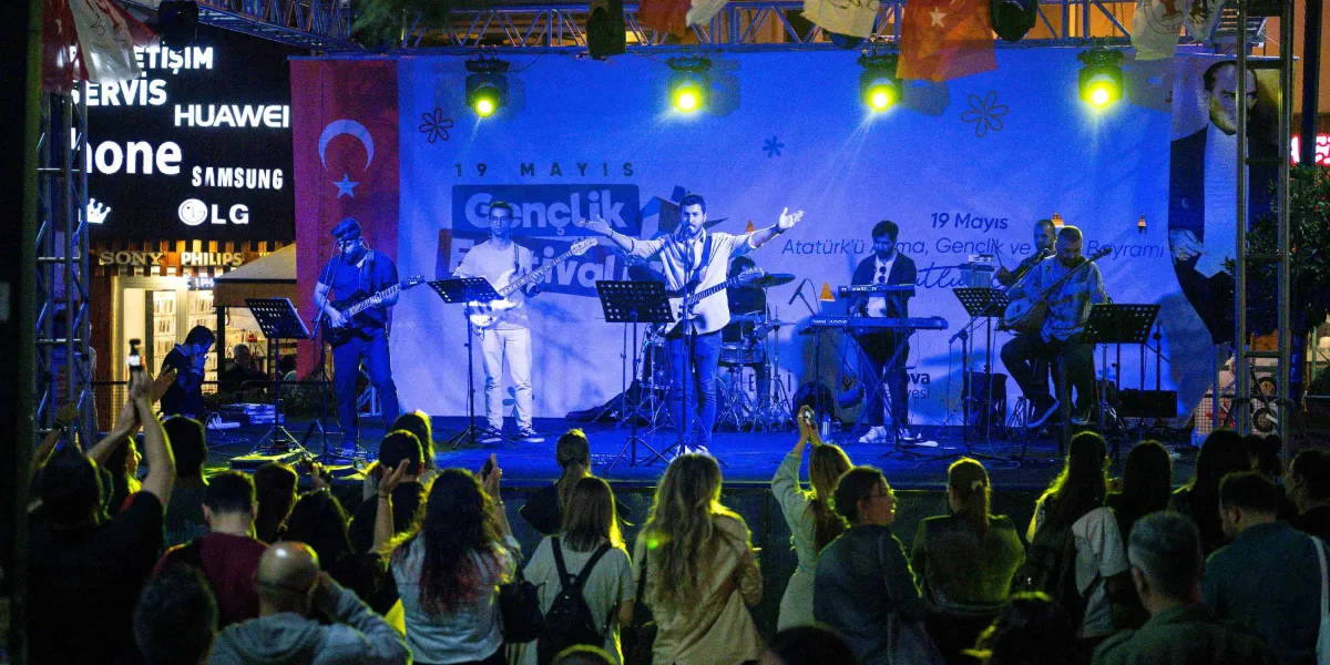 Gece vakti açık havada düzenlenen 19 Mayıs Gençlik Festivali sahnesinde, mavi ışıklar altında konser veren beş kişilik bir müzik grubu ve onları izleyen kalabalık bir kitle yer alıyor. Sahne arkasındaki dev pankartta 