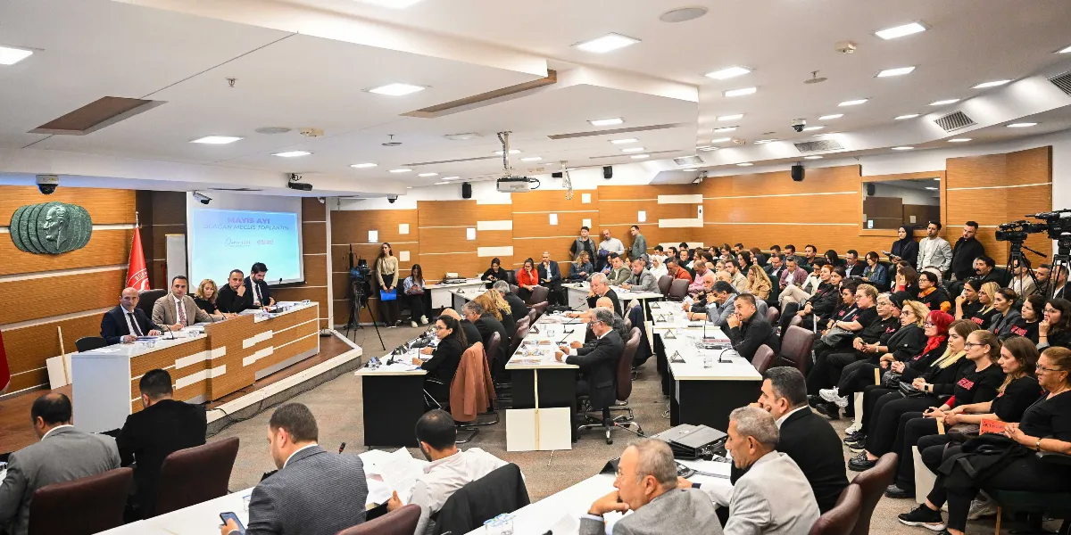 Bornova Belediyesi meclis salonunda gerçekleşen toplantıda, protokol masasında oturan yetkililer ve salonu dolduran katılımcılar yer alıyor. Salonun ön tarafındaki projeksiyon ekranında 