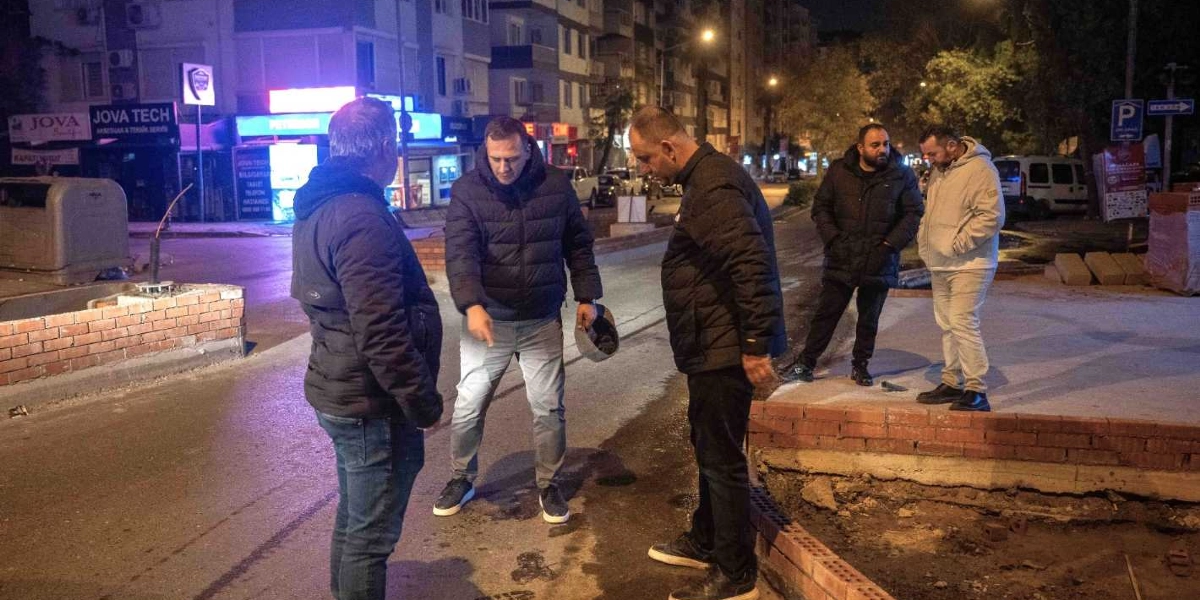 Gece vakti bir cadde üzerinde toplanmış beş kişilik bir grup, devam eden yol ve kaldırım düzenleme çalışmalarını inceliyor. Gruptaki kişilerden biri elindeki fenerle zemini işaret ederken, diğerleri onu dikkatle dinliyor. Arka planda dükkan tabelaları ve park halindeki araçların bulunduğu şehir içi bir sokak manzarası yer alıyor.