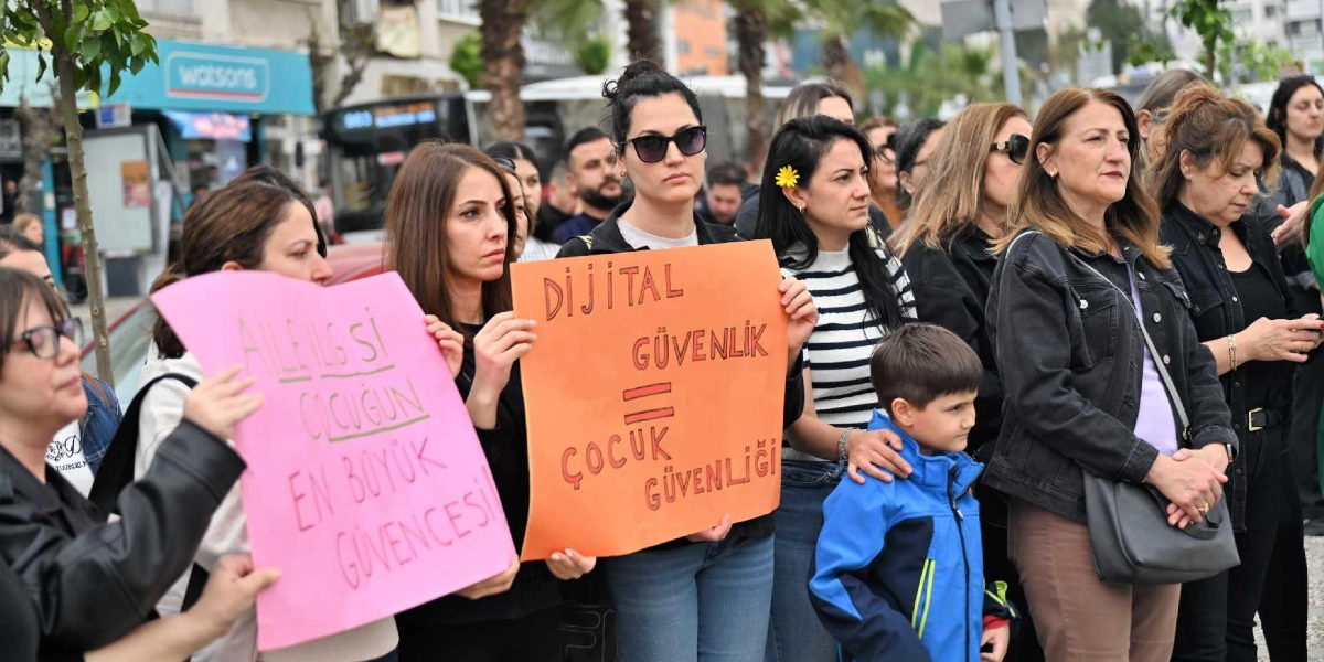 Bornova'da düzenlenen bir eylemde, ellerinde dövizler taşıyan bir grup kadın ve çocuk bir arada duruyor. Ön plandaki kadınlardan biri pembe renkli dövizde 