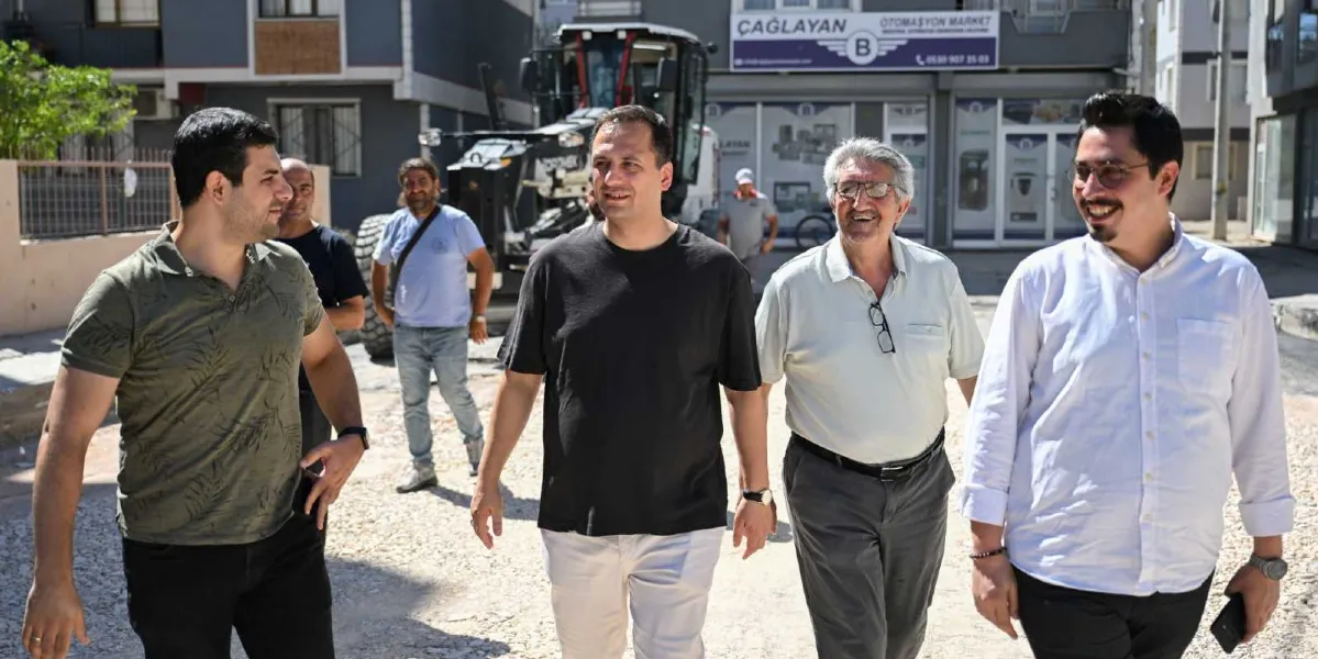 Bornova'da bir yol çalışması alanında yürüyen dört kişilik bir grup erkek, sohbet ederek ilerliyor. Önde, siyah tişörtlü bir adam, yanında beyaz gömlekli ve gözlüklü bir bey ile birlikte gülümseyerek yürüyor. Grubun hemen arkasında, üzerinde 