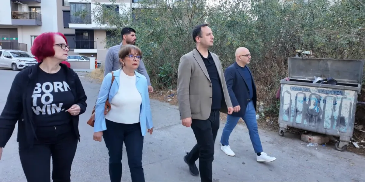 Dört kişilik bir grup, Bornova'da yerleşim alanlarının bulunduğu bir sokakta yürüyerek incelemelerde bulunuyor. Grubun önünde kırmızı saçlı, üzerinde 