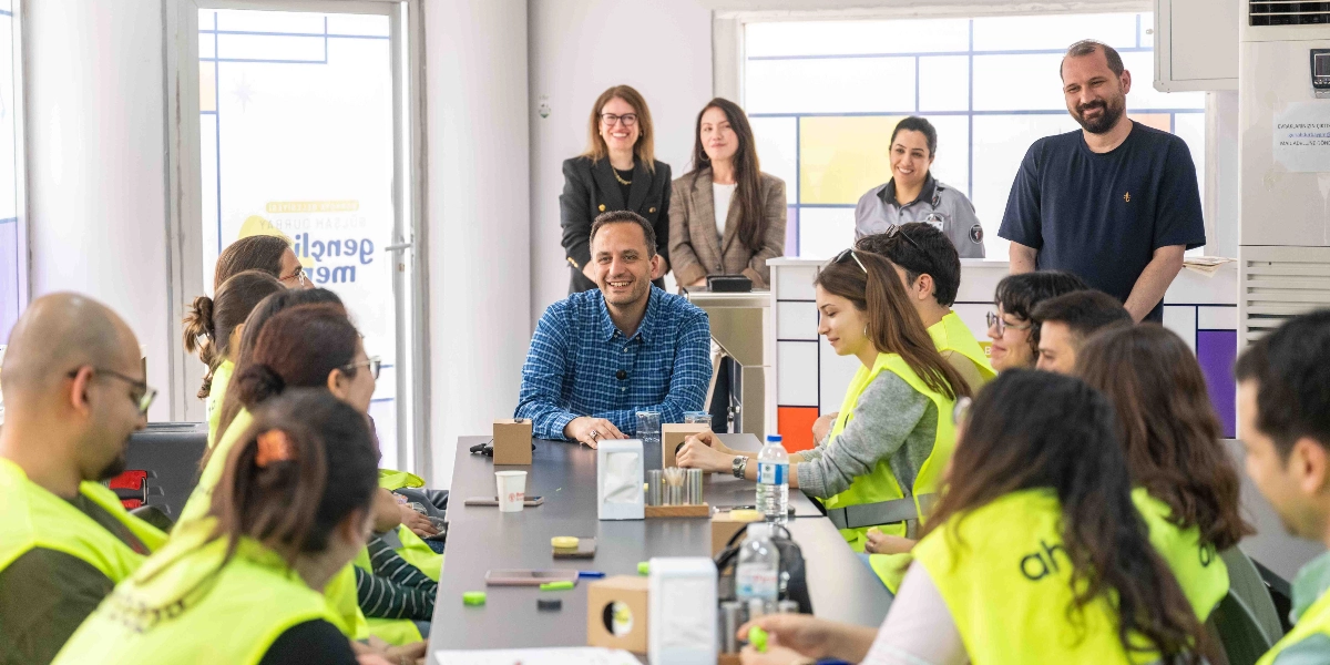 Aydınlık ve modern bir ofis ortamında, uzun bir masanın etrafında toplanmış gençlerden oluşan bir grup, Bornova Belediye Başkanı Ömer Eşki ile bir araya geliyor. Mavi kareli gömlek giyen Ömer Eşki masanın başında otururken, çevresindeki gençlerin birçoğu üzerinde 