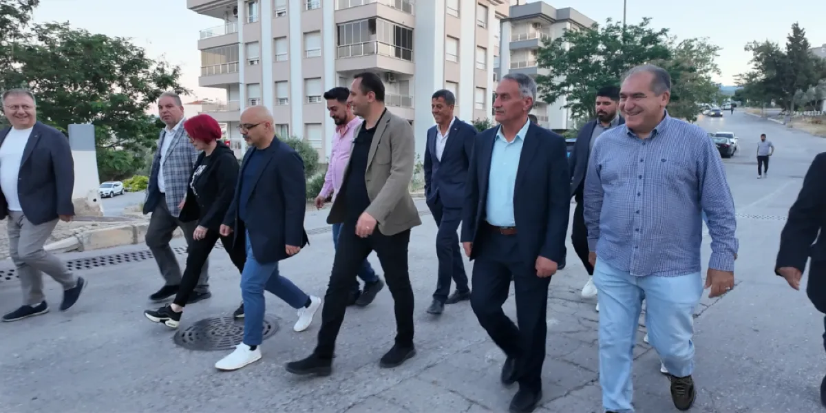 Bornova İzyuva'da bir sokakta yan yana yürüyen, çoğunluğu takım elbiseli erkeklerden ve bir kadından oluşan yaklaşık on kişilik bir grup. Grup üyeleri sohbet ederek ilerlerken, arka planda çok katlı apartmanlar ve ağaçlıklı bir yol görülüyor.