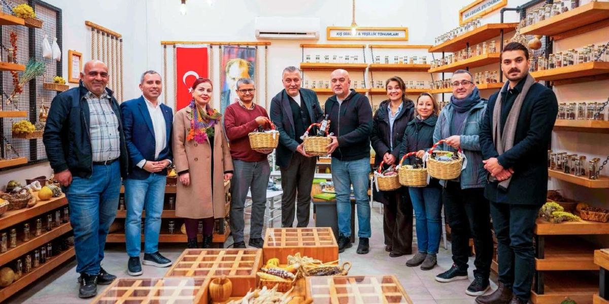Bornova'da onarıcı tarım üzerine düzenlenen bir etkinlikte, raflarında çeşitli tohum ve bitki kavanozlarının bulunduğu bir dükkanda yan yana duran on kişilik bir grup. Arka planda Türk bayrağı ve Atatürk posteri yer alıyor. Gruptaki bazı kişiler ellerinde içinde ürünler bulunan hasır sepetler tutuyor. Katılımcılar günlük kıyafetler içinde, gülümseyerek kameraya bakıyor.