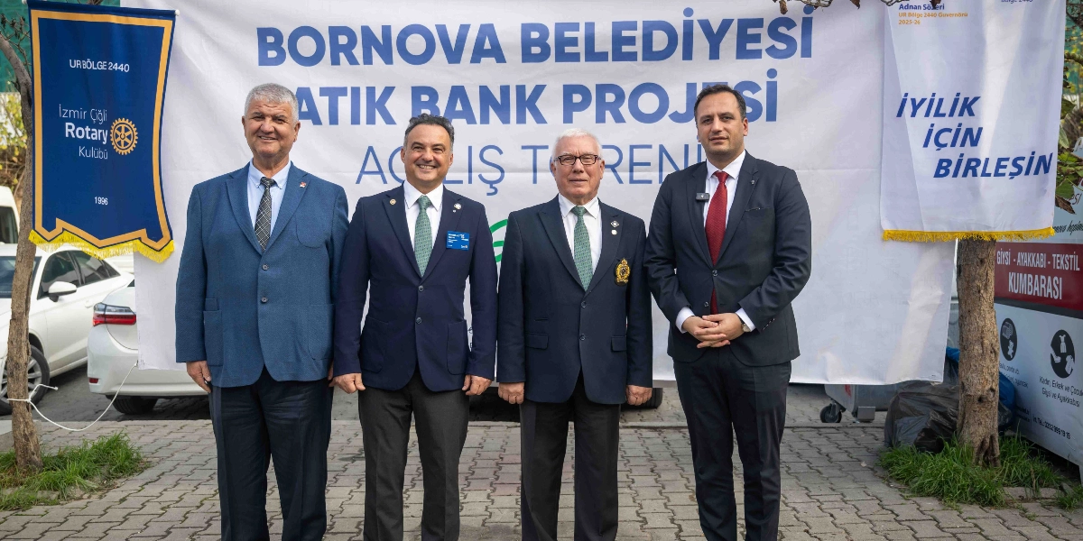 Bornova Belediyesi Atık Bank Projesi açılış töreninde, üzerinde projenin adının yazılı olduğu büyük bir pankartın önünde yan yana duran dört erkek. Soldan sağa doğru; mavi ceketli, lacivert ceketli, koyu renk ceketli ve kırmızı kravatlı koyu renk ceketli dört kişi gülümsüyor. Arka planda sağ tarafta 