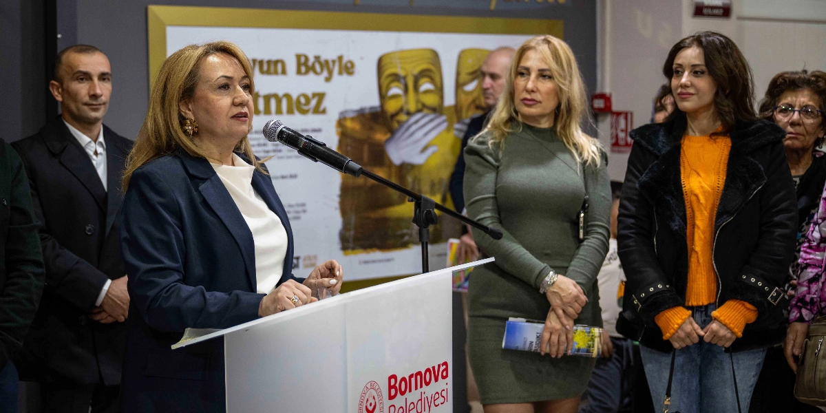 Bornova Belediyesi kürsüsünde konuşma yapan sarı saçlı bir kadın ve onu dinleyen katılımcılar. Arka planda üzerinde 