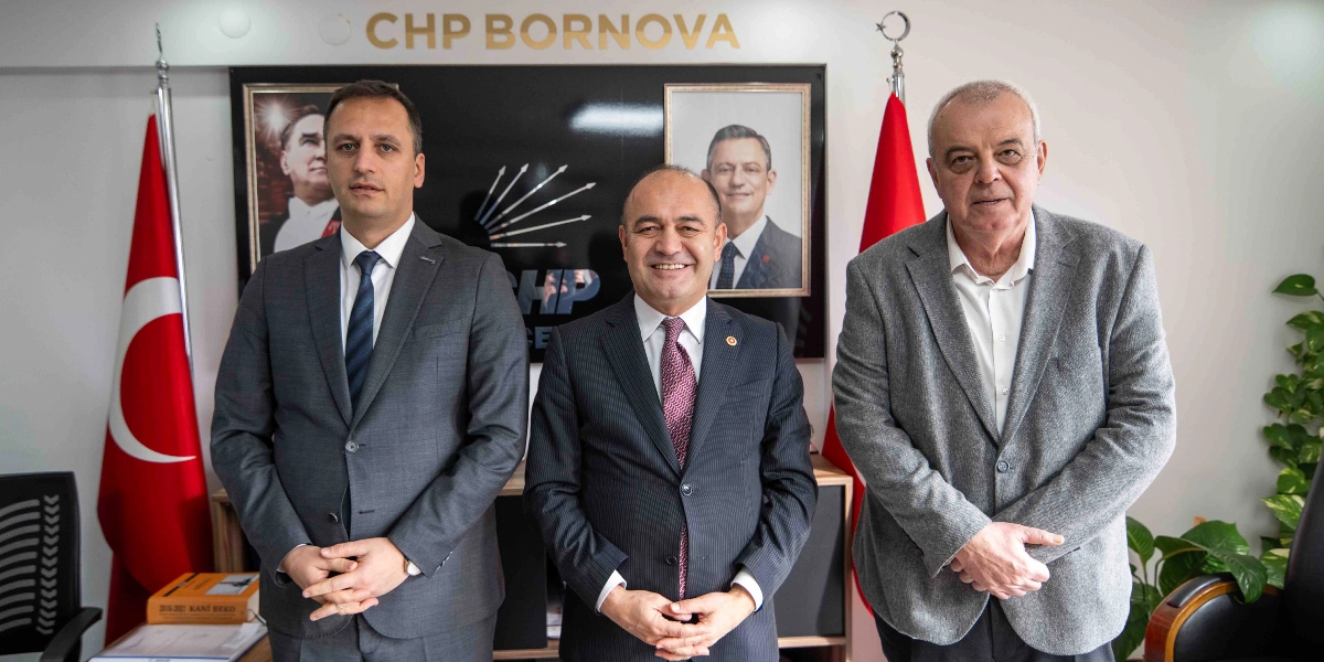 CHP Bornova ilçe binasında, arka planda Mustafa Kemal Atatürk ve Özgür Özel'in portreleri ile CHP logosunun yer aldığı duvarda, yan yana duran üç erkek siyasetçi. Ortada CHP Genel Başkan Yardımcısı Özgür Karabat, sağında ve solunda ise yerel parti temsilcileri bulunuyor. Her iki yanda Türk bayraklarının yer aldığı ortamda, siyasetçiler resmi kıyafetleriyle kameraya gülümseyerek poz veriyor.