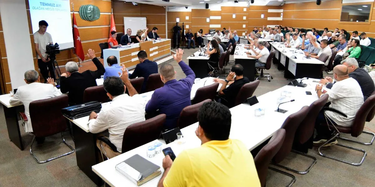 Bornova Belediyesi meclis toplantı salonunda, katılımcıların oylama yapmak için ellerini kaldırdığı bir oturum. Salonun ön tarafındaki projeksiyon ekranında 