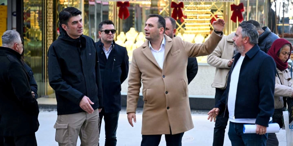 Bornova'da bir cadde üzerinde incelemelerde bulunan bir grup yetkili, ellerinde proje dosyalarıyla çevreyi gözlemliyor. Önde, bej rengi kaban giymiş bir kişi eliyle işaret ederek bir şeyler anlatırken, yanındaki siyah ceketli ve bej pantolonlu kişi onu dinliyor. Arka planda vitrininde altın takılar sergilenen bir kuyumcu dükkanı ve kırmızı başörtülü bir kadın yer alıyor.
