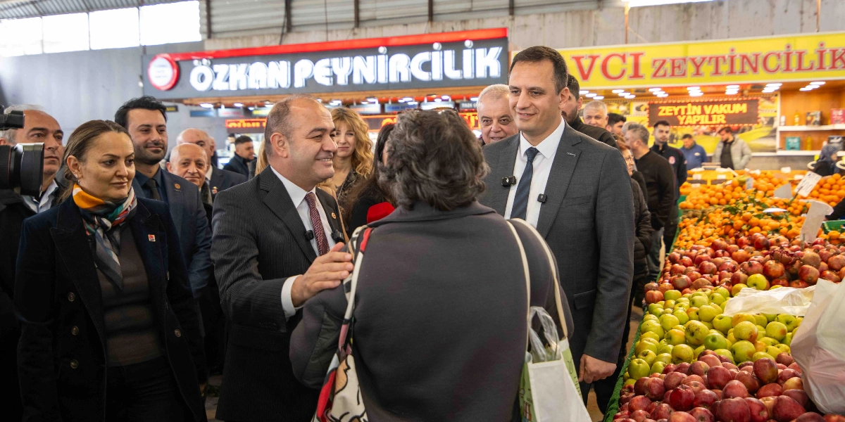 CHP Genel Başkan Yardımcısı Özgür Karabat ve beraberindeki heyet, kapalı bir pazar yerinde esnaf ve vatandaşlarla bir araya geliyor. Karabat, bir vatandaşın omzuna elini koyarak onunla sohbet ederken, yanında takım elbiseli diğer yetkililer ve arka planda 