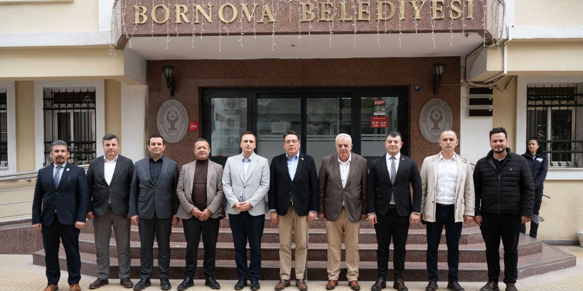 Bornova Belediyesi binasının önünde, yan yana dizilmiş on kişilik bir grup erkek, resmi ve yarı resmi kıyafetlerle objektife bakıyor. Arka planda belediye binasının girişi ve üzerinde 