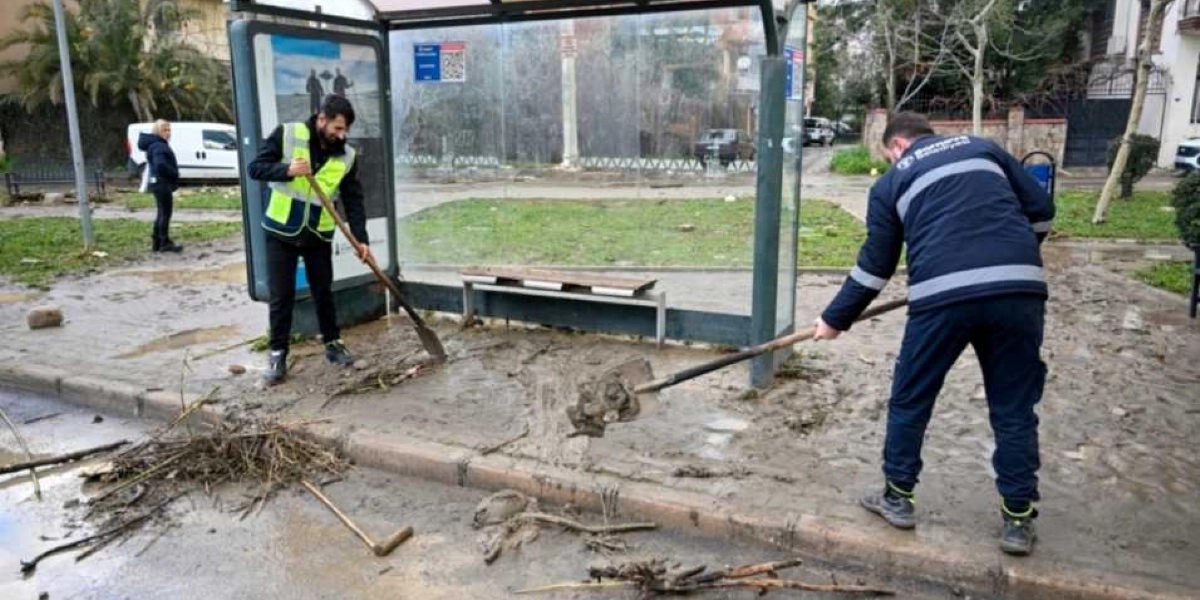 Bornova Belediyesi personeli, sel sonrası otobüs durağının çevresinde ve içinde biriken çamur ve atıkları küreklerle temizliyor.