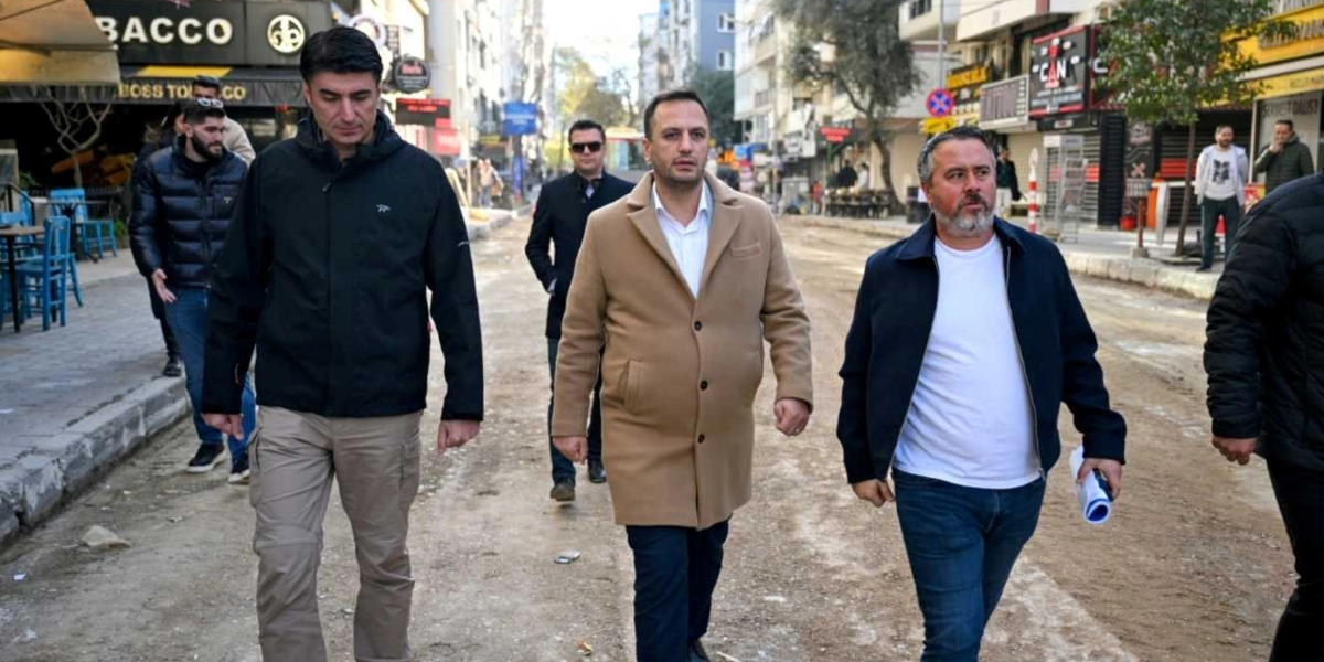 Bornova'da devam eden altyapı ve üstyapı çalışmalarının sürdüğü bir caddede yürüyen, aralarında Bornova Belediye Başkanı Mustafa İduğ'un da bulunduğu bir grup yetkili. Yetkililer, toprak ve taşlarla kaplı, düzenleme aşamasındaki caddede incelemelerde bulunuyor.