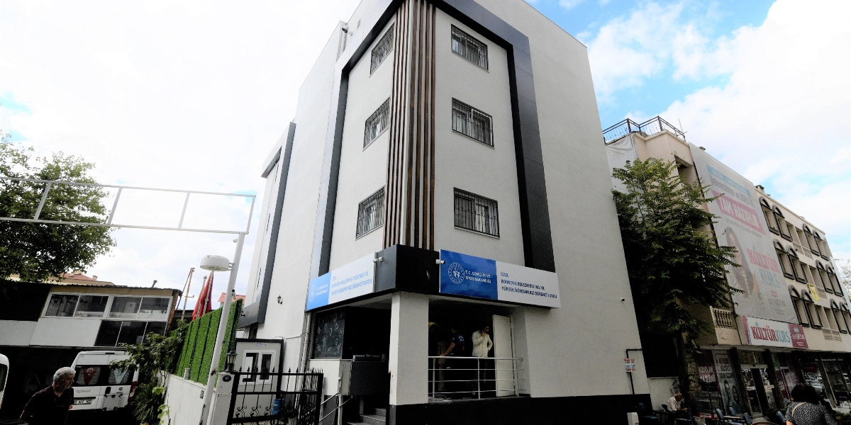 Beyaz ve siyah detaylara sahip, dört katlı modern bir binanın dış görünüşü. Binanın girişinde T.C. Gençlik ve Spor Bakanlığı logosunun yer aldığı ve üzerinde 