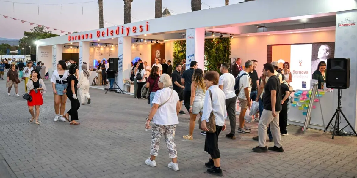 İzmir Enternasyonal Fuarı'nda yer alan Bornova Belediyesi standının önünde yürüyen ve standı ziyaret eden kalabalık bir insan grubu. Modern tasarımlı, üzerinde 