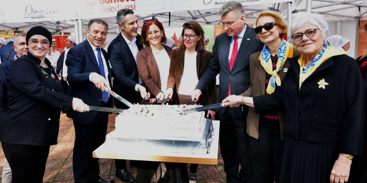 Bornova Belediyesi'nin düzenlediği bir etkinlikte, aralarında Bornova Belediye Başkanı'nın da bulunduğu bir grup yetkili, beyaz kremalı büyük bir pastayı birlikte kesiyor. Arka planda Bornova Belediyesi logolu beyaz çadırlar yer alıyor.