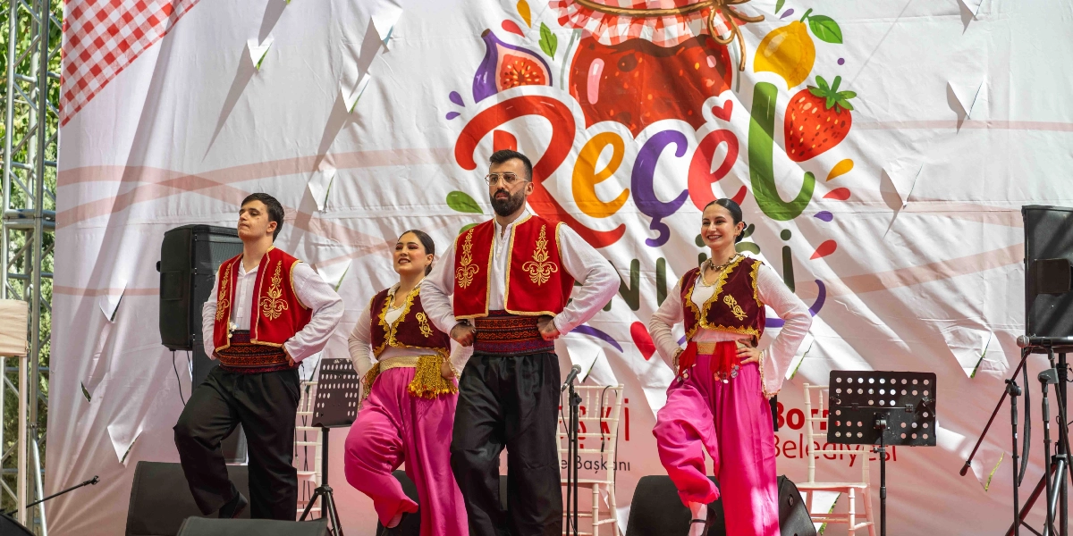 Geleneksel kıyafetler giymiş iki erkek ve iki kadın dansçı, arkalarında 