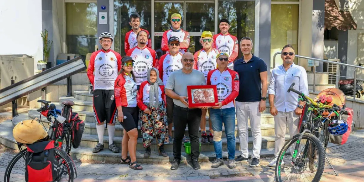 Büyük Taarruz Bisiklet Turu'na katılan bir grup bisikletçi, bir bina girişindeki merdivenlerin önünde yan yana duruyor. Grubun bir kısmı üzerinde 