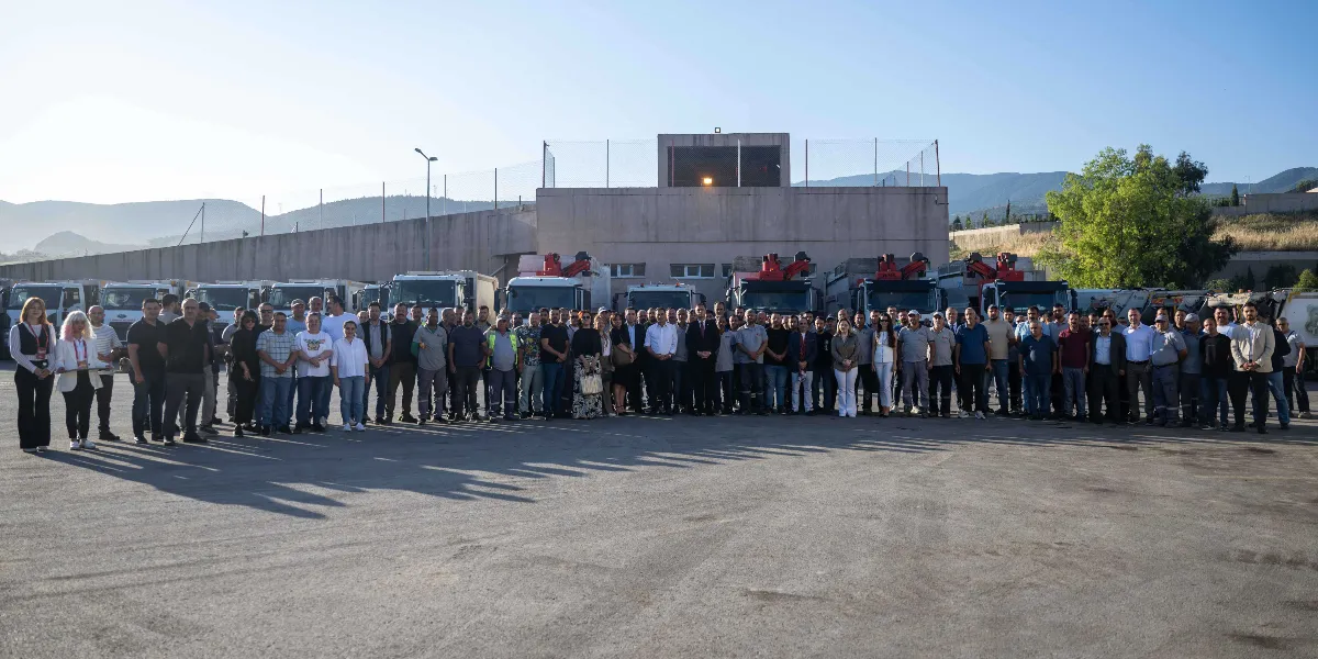 Açık havada, arkalarında sıralanmış çok sayıda iş makinesi ve kamyon bulunan geniş bir alanda yan yana duran, aralarında Bornova Belediyesi çalışanlarının da bulunduğu kalabalık bir grup insan toplu fotoğraf çektiriyor.