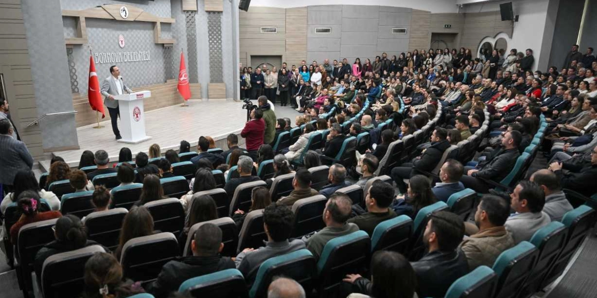 Bornova Belediyesi'nin konferans salonunda, kürsüde konuşma yapan Başkan Ömer Eşki ve onu dinleyen kalabalık bir belediye personeli grubu. Salonun sahne kısmında Türk bayrağı ve Bornova Belediyesi flaması yer alırken, izleyiciler kademeli koltuklarda oturarak etkinliği takip ediyor.