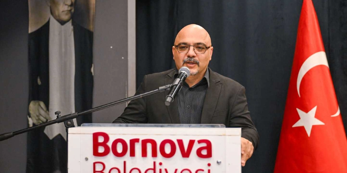 Bornova Belediyesi kürsüsünde konuşma yapan, gözlüklü, kel ve bıyıklı bir erkek. Arka planda sol tarafta Mustafa Kemal Atatürk'ün bir portresi, sağ tarafta ise Türk bayrağı yer alıyor.