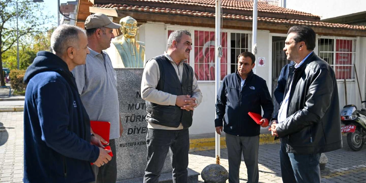 Açık havada, bir muhtarlık binasının önünde duran beş kişilik bir grup erkek, birbirleriyle sohbet ediyor. Grubun arkasında, üzerinde Mustafa Kemal Atatürk'ün büstünün bulunduğu gri bir kaide yer alıyor. Kaidenin üzerinde 