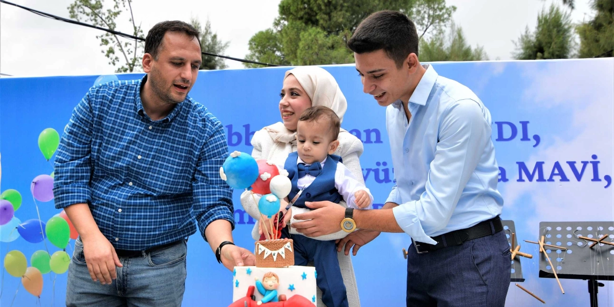 Mavi kareli gömlekli bir erkek, beyaz kıyafetli ve başörtülü bir kadın ve açık mavi gömlekli genç bir erkek, üzerinde 