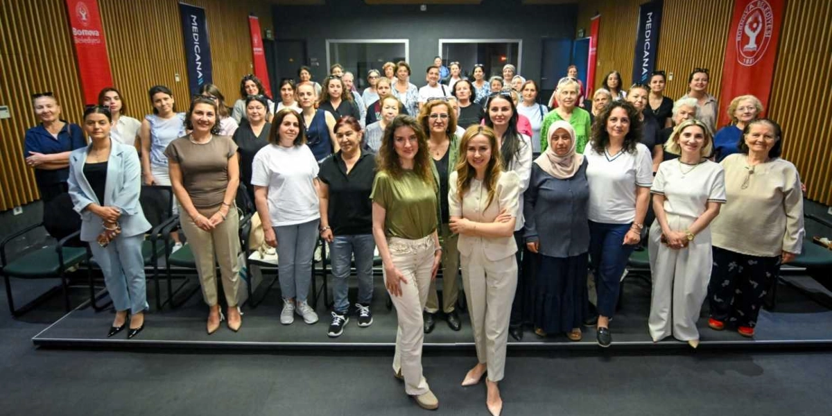 Bornova Belediyesi tarafından düzenlenen bir etkinlikte, anneliğin görünmeyen yükü üzerine yapılan toplantıya katılan çok sayıda kadın, konferans salonunda yan yana durarak toplu fotoğraf çektiriyor. Ön planda iki kadın konuşmacı yer alırken, arkalarında farklı yaş gruplarından katılımcılar bulunuyor. Salonun arka duvarında Bornova Belediyesi ve Medicana logolarının yer aldığı dikey afişler asılı.
