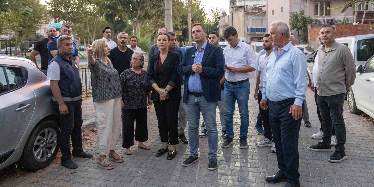 Sabahın erken saatlerinde Bornova'da bir sokakta toplanmış, aralarında Bornova Belediye Başkanı Ömer Eşki'nin de bulunduğu bir grup yetkili ve vatandaş, çevreyi inceleyerek sohbet ediyor. Gruptaki bir kadın eliyle bir noktayı işaret ederek açıklamalarda bulunurken, diğerleri onu dinliyor. Çoğunluğu erkeklerden oluşan grup, günlük kıyafetler içinde parke taşlı bir yol üzerinde duruyor; arka planda ise ağaçlar, park edilmiş araçlar ve binalar yer alıyor.
