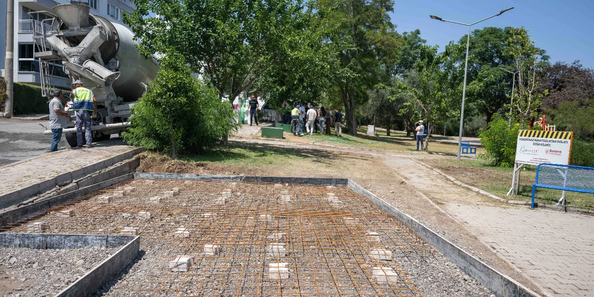 Bornova Belediyesi tarafından yürütülen bir inşaat çalışmasında, beton dökümü için hazırlanmış demir donatılı zemin ve yanında bekleyen bir beton mikseri görülüyor. Arka planda ağaçlık bir alan, yürüyüş yolu ve çevrede duran insanlar yer alıyor. Sağ tarafta ise üzerinde 