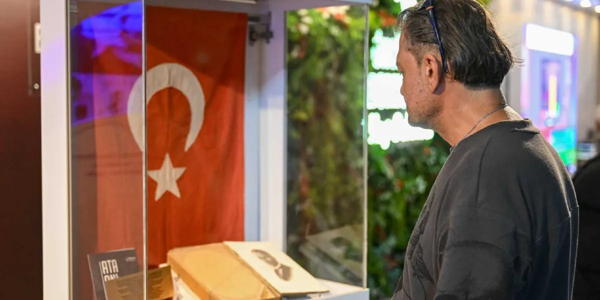 İzmir Enternasyonal Fuarı'ndaki Bornova Belediyesi standında, cam bir vitrin içerisinde sergilenen Türk bayrağını ve Mustafa Kemal Atatürk'e ait olduğu anlaşılan tarihi belgeleri inceleyen orta yaşlı bir erkek.