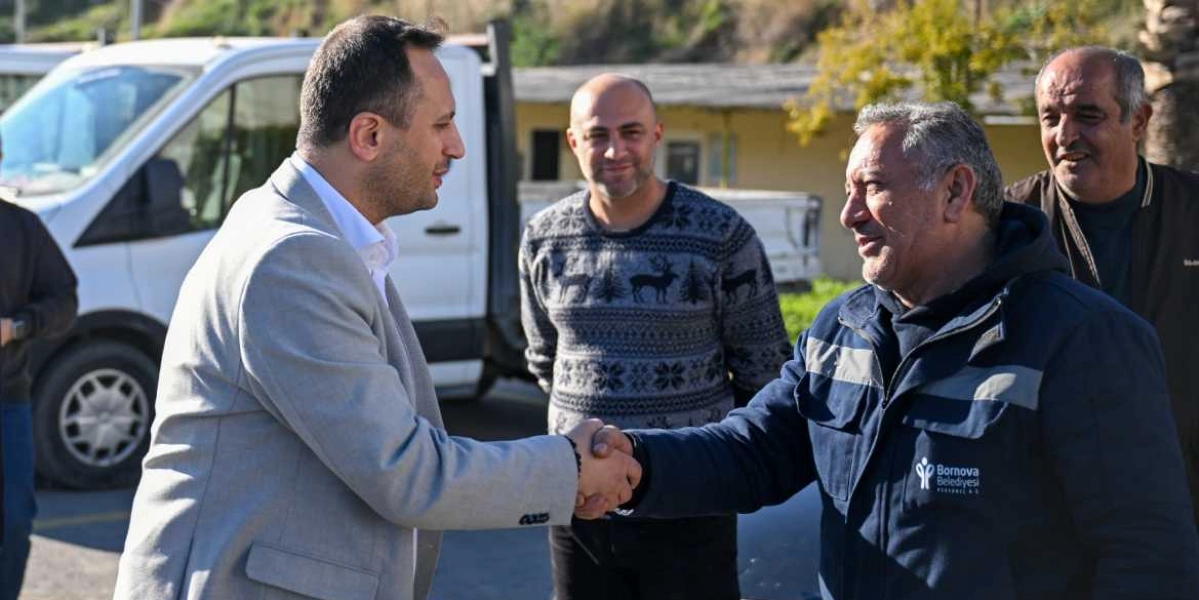 Gri ceketli bir yetkili, üzerinde Bornova Belediyesi Personel A.Ş. logosu bulunan lacivert iş kıyafetli bir çalışanla el sıkışıyor. Arka planda gülümseyerek onları izleyen iki kişi daha bulunuyor ve ortamda beyaz bir hizmet aracı yer alıyor.