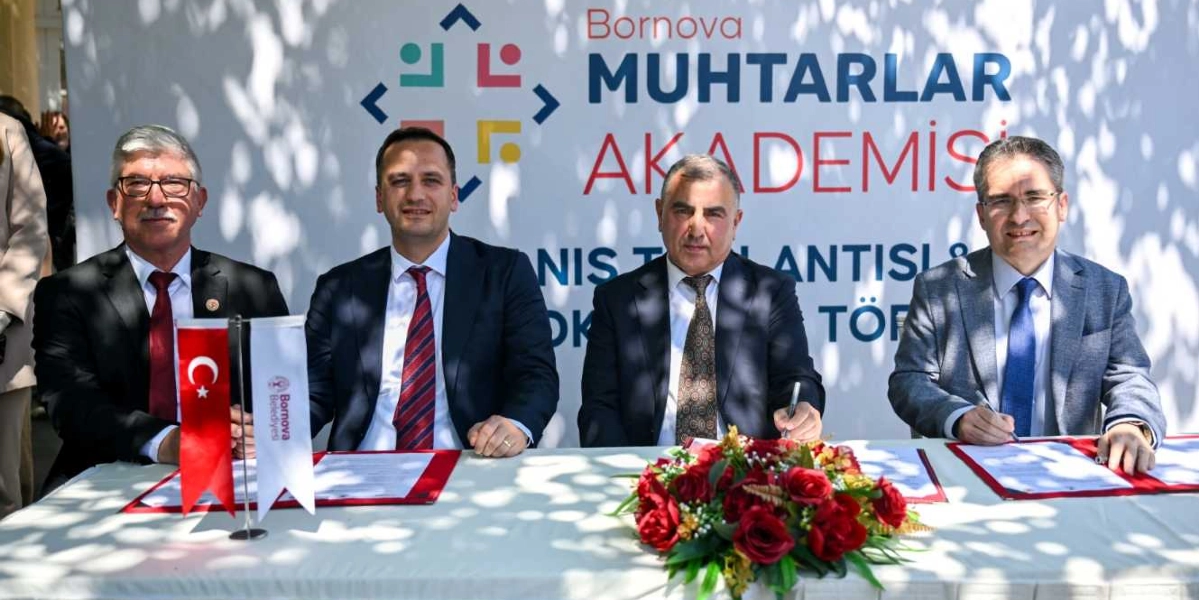 Beyaz bir masa etrafında yan yana oturan dört erkek, önlerindeki belgeleri imzalıyor. Arka planda 
