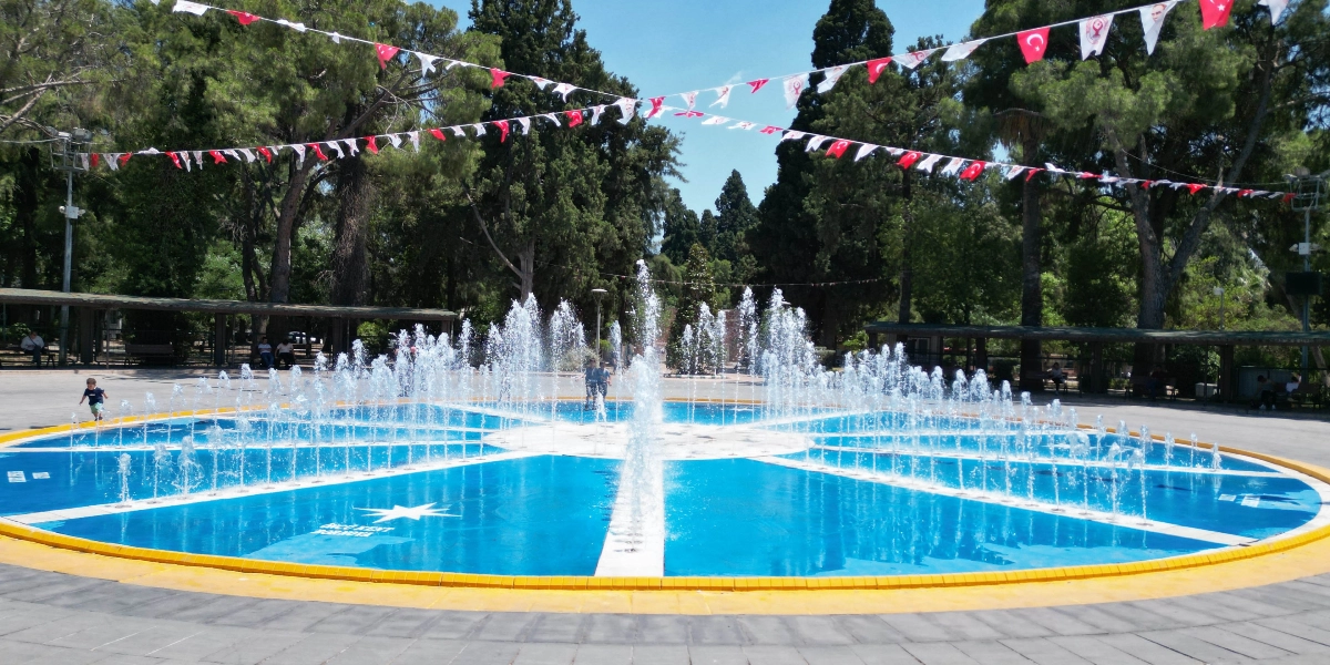 Ağaçlarla çevrili bir parkın ortasında, dairesel formda, parlak mavi zeminli ve fıskiyeli bir süs havuzu yer alıyor. Havuzun zemininde beyaz renkli bir yıldız figürü ve 