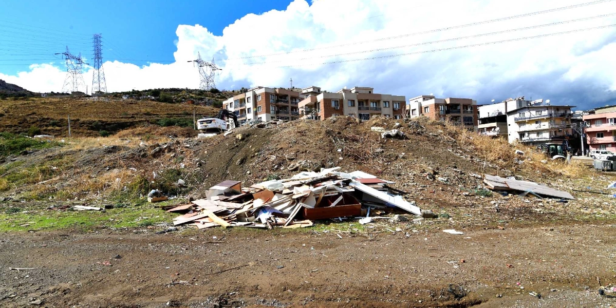 Arka planda çok katlı apartmanların ve yüksek gerilim hatlarının bulunduğu, ön planda ise toprak bir zemin üzerinde inşaat atıkları ve moloz yığınlarının yer aldığı boş bir arazi.