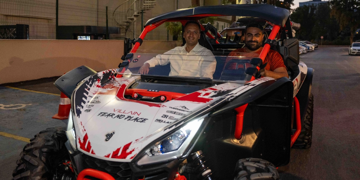Beyaz ve kırmızı renkli, üzerinde Villain ve Fear No Place yazıları bulunan off-road aracının içinde oturan iki erkek, kameraya gülümseyerek bakıyor. Araç, dış mekanda, park alanında bulunuyor.