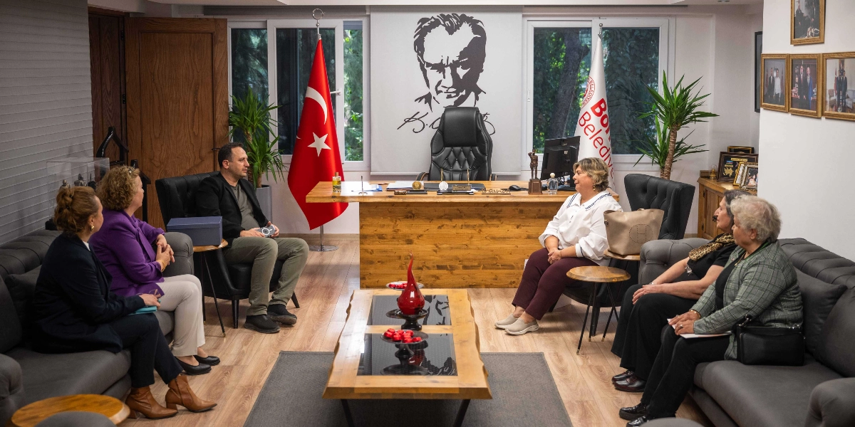 Bornova Belediye Başkanı'nın makam odasında gerçekleşen bir toplantıda, bir erkek ve beş kadın karşılıklı koltuklarda oturarak sohbet ediyor. Odanın arka planında, merkezde Mustafa Kemal Atatürk'ün büyük bir portresi, yanında Türk bayrağı ve Bornova Belediyesi'nin flaması yer alıyor. Ahşap bir çalışma masasının önünde, ortada cam detaylı ahşap bir sehpa bulunuyor. Duvarlarda ise çeşitli fotoğraflar asılı.