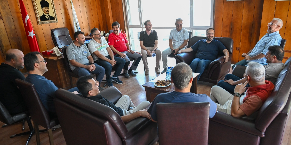 Ahmet Eşki, 3. Sanayi Sitesi'ndeki bir ofiste, aralarında sanayi sitesi yöneticilerinin de bulunduğu bir grupla bir araya gelerek sohbet ediyor. Ahşap panellerle kaplı odada, deri koltuklarda oturan grup üyeleri samimi bir ortamda gülümseyerek konuşuyor. Odanın duvarında Mustafa Kemal Atatürk'ün portresi ve yanında Türk bayrağı yer alıyor. Orta kısımdaki masada su şişeleri ve bir tabak kurabiye bulunuyor.