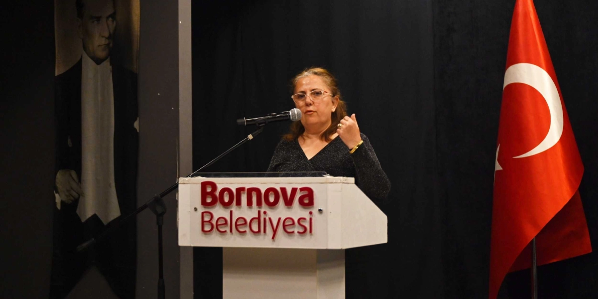 Bornova Belediyesi kürsüsünde konuşma yapan, gözlüklü ve siyah kıyafetli bir kadın. Kürsünün sol tarafında Mustafa Kemal Atatürk'ün portresi, sağ tarafında ise Türk bayrağı yer alıyor.