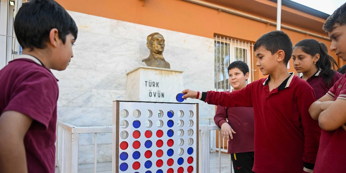 Bordo okul forması giyen bir grup öğrenci, okul bahçesinde dev boyutta bir 