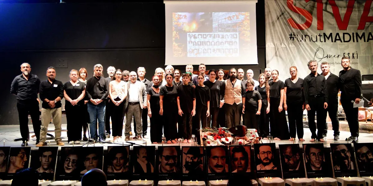 Kapalı bir sahnede, Madımak Oteli yangınında hayatını kaybedenlerin anısına düzenlenen bir etkinlikte, siyah giyinmiş bir grup insan sahne üzerinde yan yana duruyor. Arka planda, üzerinde Madımak Oteli'nin yanan görüntüsü ve kurbanların fotoğraflarının yer aldığı bir projeksiyon perdesi ile 