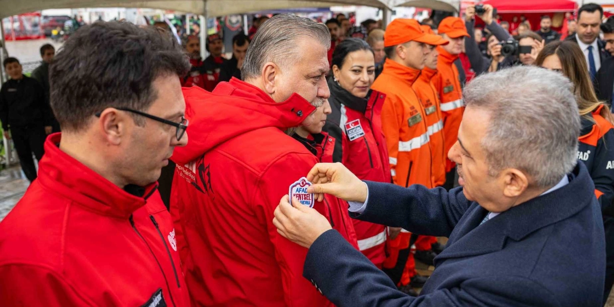 Koyu renkli takım elbiseli bir yetkili, kırmızı renkli arama kurtarma üniforması giyen bir görevlinin koluna 